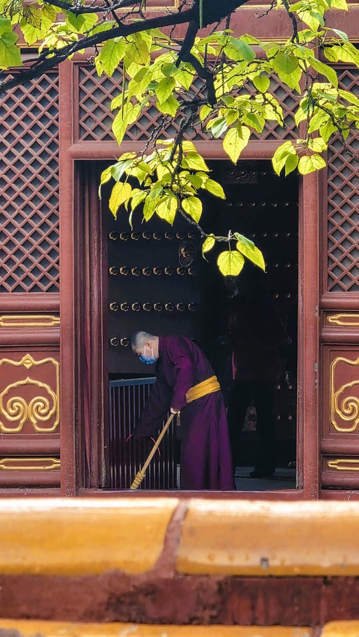 Serene image of a monk sweeping at a temple in Beijing, surrounded by vibrant spring foliage.
