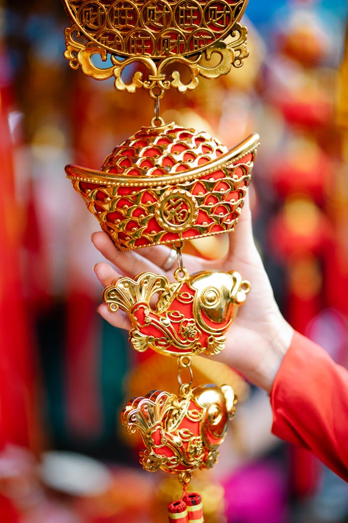Crop anonymous female touching traditional ornamental red and golden decoration with fish and sycee hanging in local street market during Chinese New Year holidays